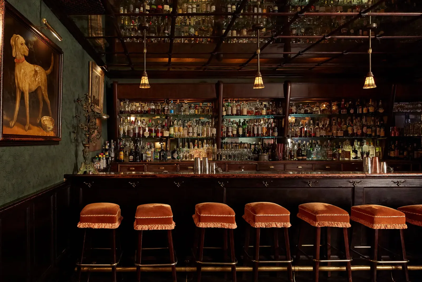 The Bowery Lobby bar with a long dark counter, backlit bottles, and leather stools