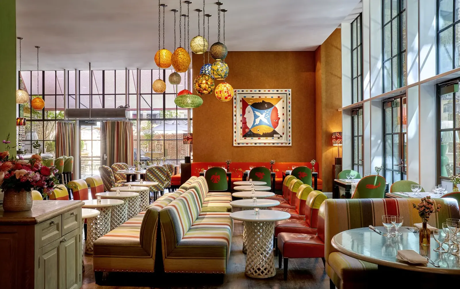 A bright Crosby Bar seating area with striped banquettes, colorful pendant lights, and floor to ceiling windows