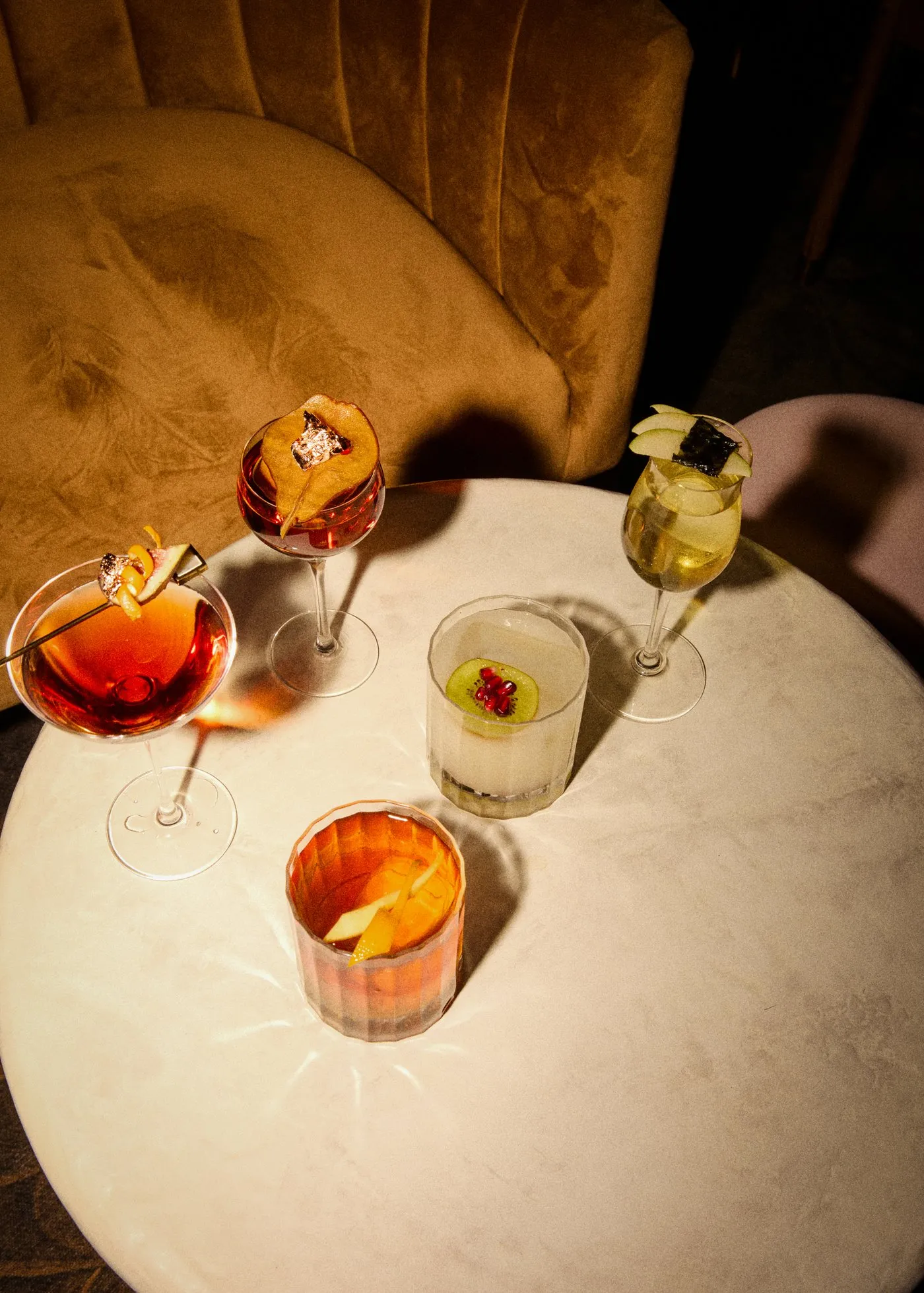 A selection of cocktails on a small round table beside upholstered seating at Dandelion