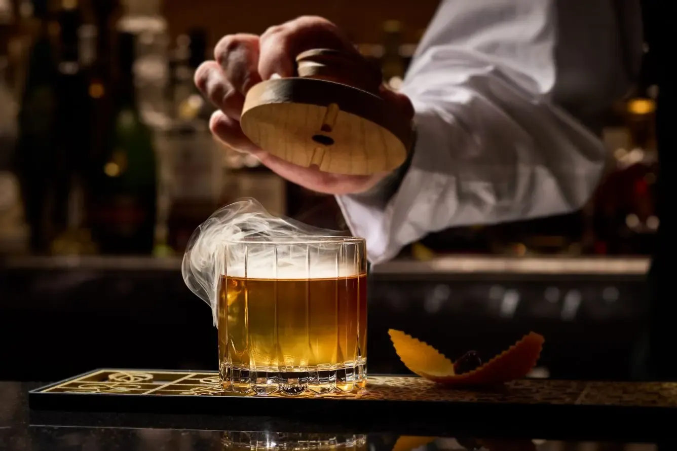 A bartender pouring a stirred amber cocktail over ice at The St. Regis New York