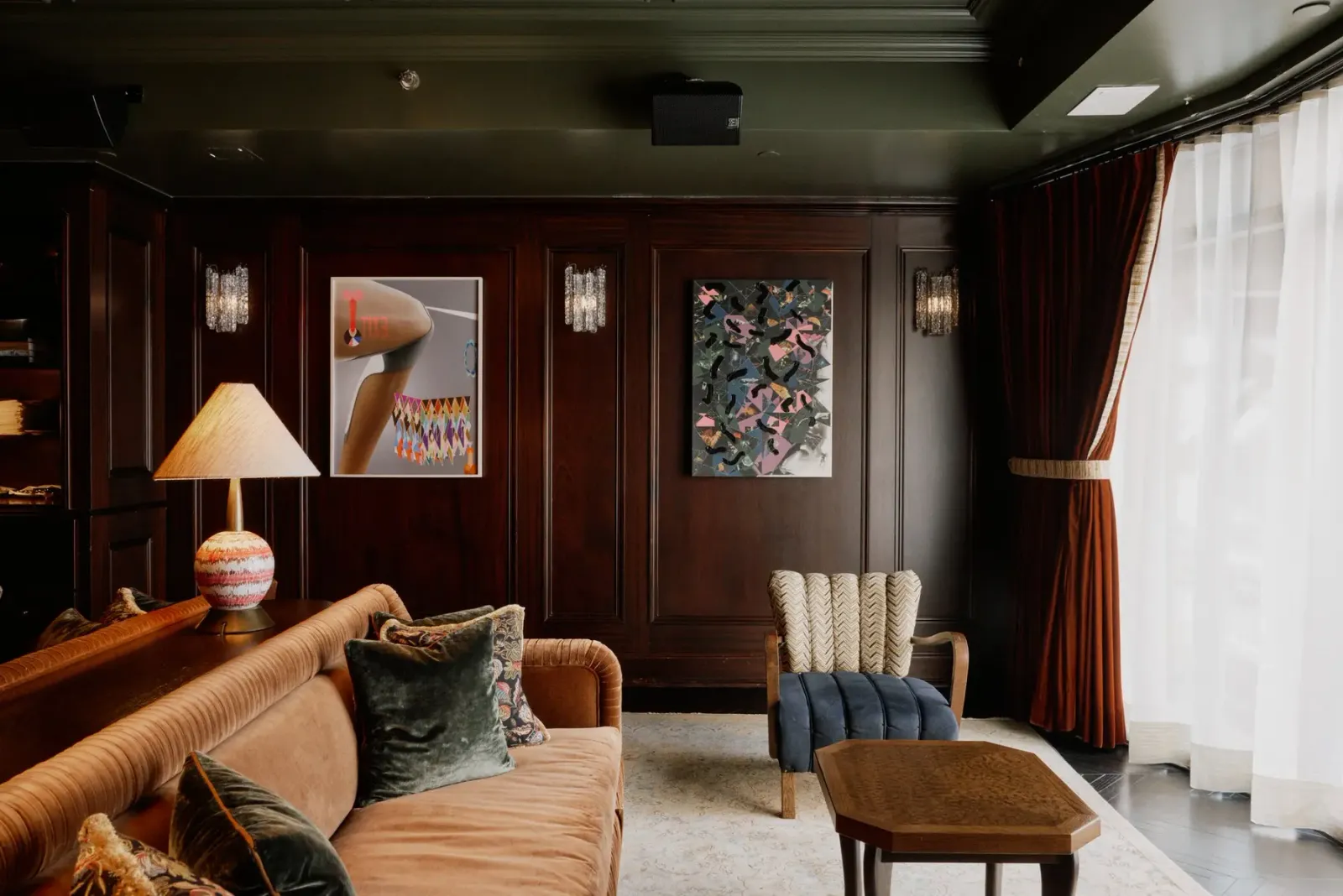 A paneled sitting area at Little Ned with a curved leather sofa, low tables, framed art, and tall windows