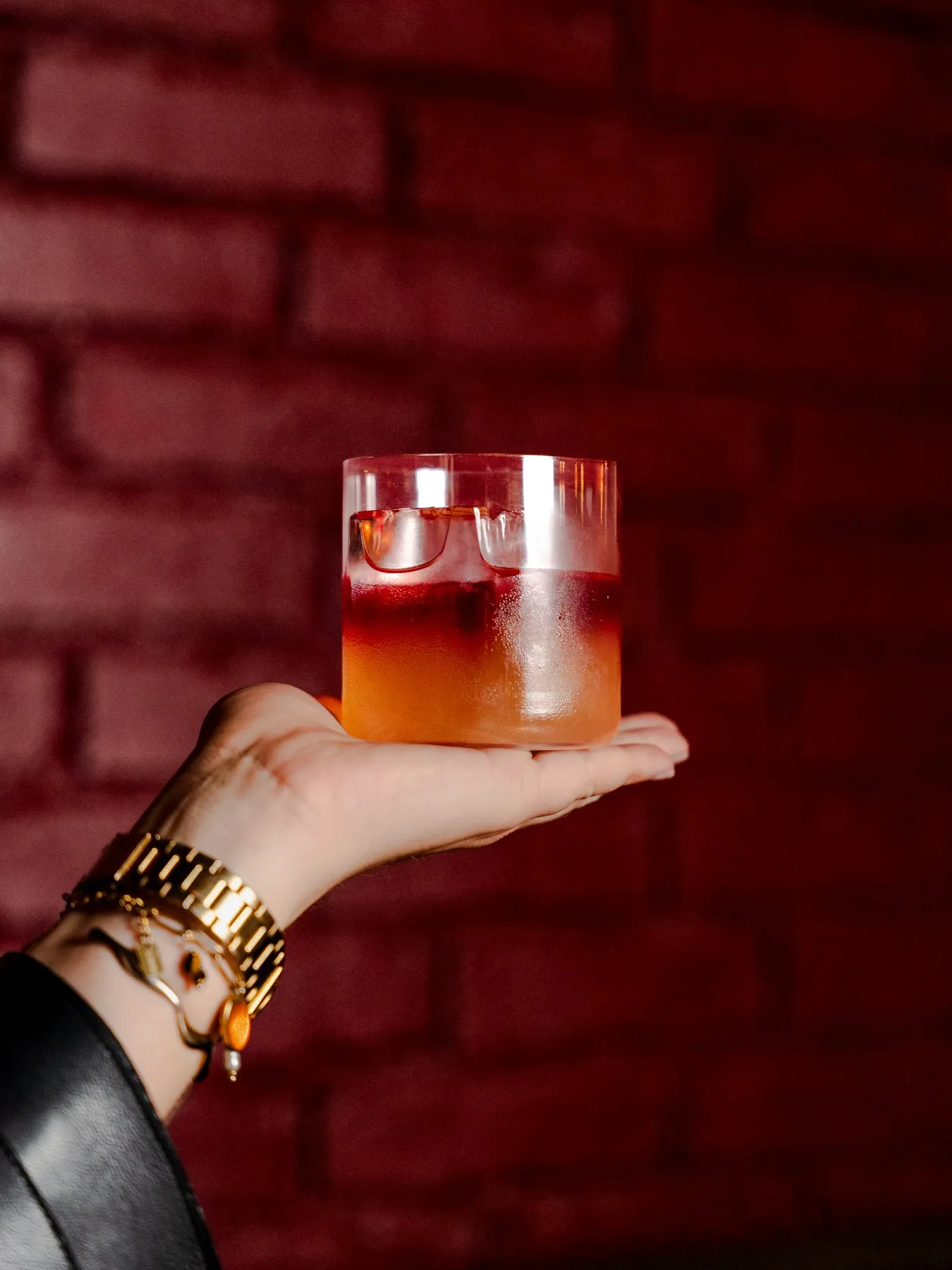 A cocktail in a rocks glass against a red brick backdrop at Saint